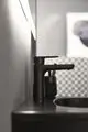 Schwarze Waschtischarmatur von Ideal Standard, mit schlichter Gestaltung, montiert auf glatter Oberfläche, im Hintergrund eine strukturierte Wand und reflektierenden Elementen.